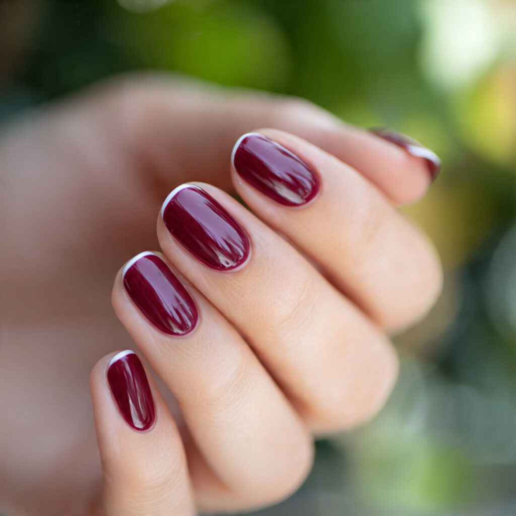 one hand with burgundy gloss french tip manicure e